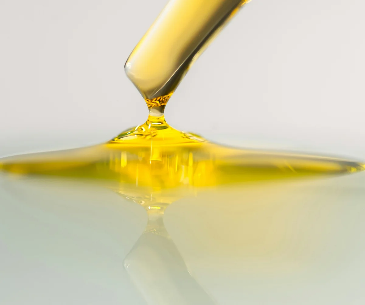 Olio cosmetico dorato versato da un contagocce su superficie riflettente